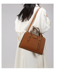 Detail of caramel tote bag showing golden hardware and texture on white trench coat