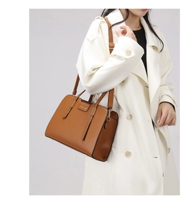 Caramel brown leather tote bag worn with a white trench coat in a studio detail shot