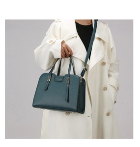 Close-up of dark green textured leather handbag with gold accents and fashion lettering