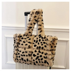 Quilted cow print plush tote bag hanging on a suitcase handle in a minimalist setting