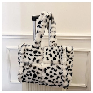 Detail of plush faux fur cow print handbag hanging on white suitcase handle