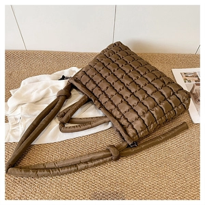 Détail de la texture d'un sac cabas matelassé marron avec anses rembourrées sur un tapis