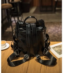 Detail of black glossy backpack with diamond quilting and side pocket on wooden table