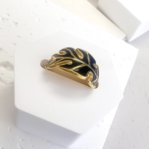 Macro detail of gold palm leaf ring with dark blue enamel inlay on a white stand
