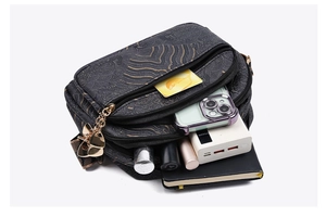 Crossbody bag detail showing three separate zipper pockets and gold jacquard pattern