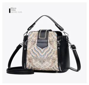 Side view of black leather crossbody bag featuring beige ethnic embroidery and metal zippers