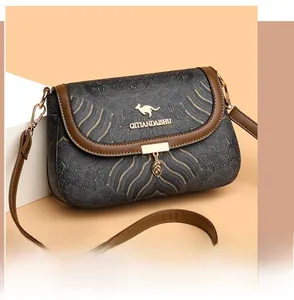 Detail of dark grey textured crossbody bag with brown trim and leaf-shaped metal pendant
