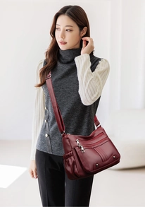 Détail du sac en cuir bordeaux avec plusieurs poches zippées et une bandoulière réglable