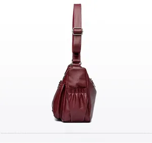 Détail d'un sac à bandoulière en cuir bordeaux montrant les poches latérales zippées
