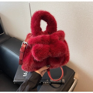 Detail of plush red faux fur bucket bag featuring fluffy pom-poms and adjustable strap