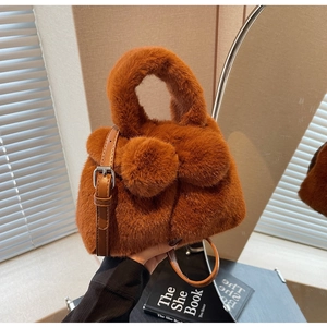 Detailed close-up of soft brown faux fur bucket bag with plush pom-pom decorations