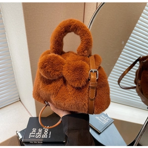 Detail of plush brown bucket bag showing fuzzy texture, pom-pom decor and leather handle