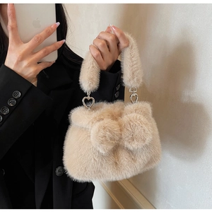 Close-up of beige faux fur bucket bag with heart metal buckle and fluffy pom-poms