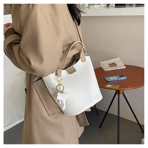 Detalle de bolso tipo cubo de cuero blanco con asa marrón y colgante de elefante