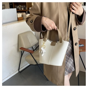 Detalle del bolso de cubo blanco con patrón de litchi, asas marrones y dije de caballo
