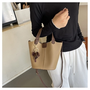 Detalle del bolso tipo cubo de cuero caqui con asa marrón y amuleto de flor decorativo