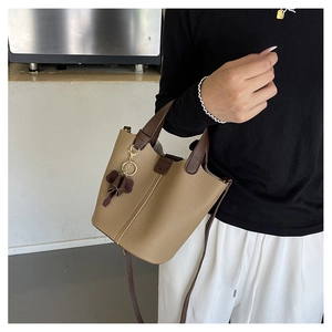 Primer plano del bolso cubo caqui en cuero granulado con colgante de flor marrón