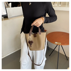 Detalle de bolso cubo de cuero granulado marrón con asa oscura y colgante de osito