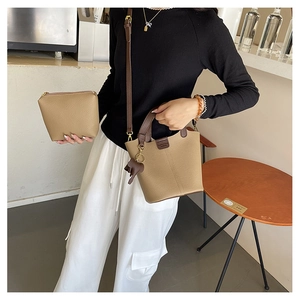 Detalle de un bolso tipo cubo beige con correas marrones y un colgante de elefante de cuero