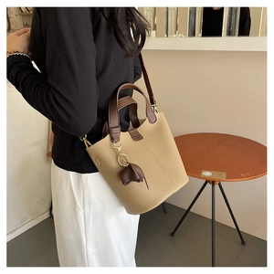 Detalle del bolso de cubo beige granulado con asa de cuero marrón y colgante de elefante