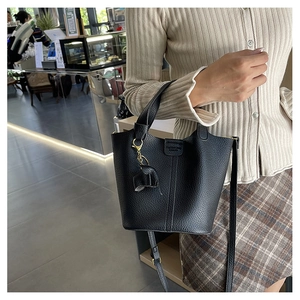 Detalle de bolso tipo cubo de cuero negro con asa superior y colgante de elefante