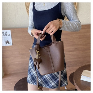 Detalle de bolso cubo de cuero marrón con patrón de lichi y colgante de elefante