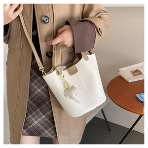 Detalle del bolso de cubo blanco con textura de grano, colgante elefante y asa de cuero