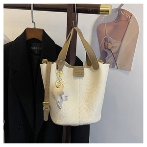 Detalle del bolso de cubo en cuero blanco con colgante de elefante dorado y un asa