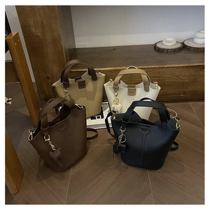 Selección de bolsos tipo cubo en cuero granulado marrón, beige, crema y negro sobre madera