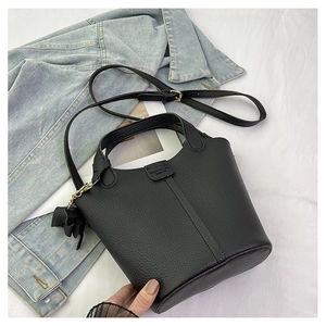 Detalle del bolso tipo cubo negro en cuero con asas y un colgante de borla decorativo