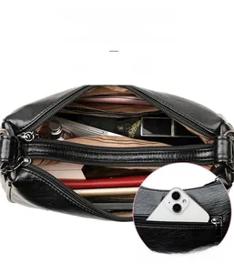 Macro detail of black leather crossbody bag featuring multiple zipper compartments and texture
