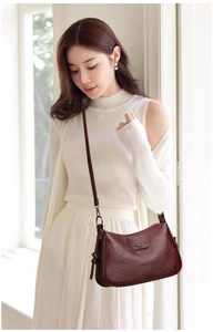 Side view of a wine red crescent crossbody bag with metallic kangaroo logo on model