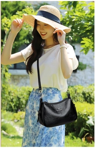 Detail of elegant black leather crossbody bag with kangaroo logo shown in outdoor garden