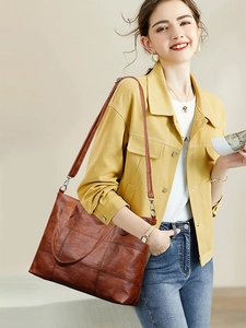 Detail shot of a brown pebbled leather tote bag with square stitching on a model