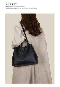 Model wearing a black top grain oil wax leather tote bag with woven handles on a beige coat
