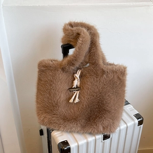 Brown faux fur tote bag with toggle closure on a white suitcase in a clean setting