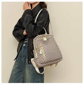 Detail view of a beige checkered backpack with gold zippers worn on model's shoulder