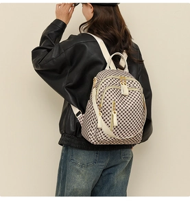 Detail of checkered pattern travel backpack with white straps and multiple zipper pockets