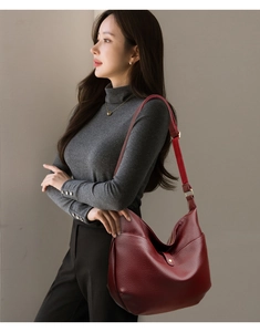 Detail of burgundy lychee-pattern leather hobo bag with gold metal buckle and strap