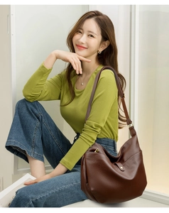 Detail of dark brown pebble leather shoulder bag with wide strap and gold zipper on a model