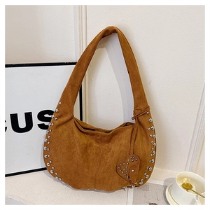 Detail of brown suede crescent bag featuring silver studs and a heart charm accessory