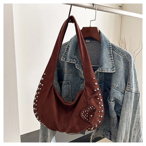 Detailed view of brown suede shoulder bag with silver rivets and heart charm on denim
