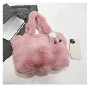 Detailed view of a pink plush faux fur tote bag with a white pompom on a soft bed