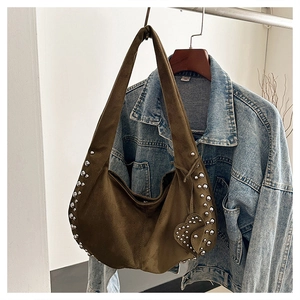 Detail of dark brown suede crescent bag with silver rivets against a denim jacket