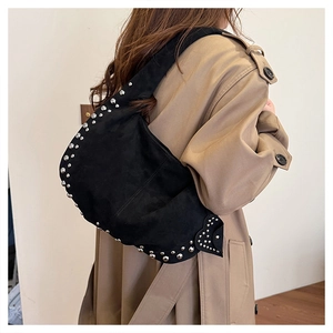Detail of black suede crescent bag with silver rivet trim worn with a khaki trench coat