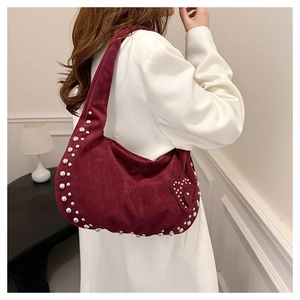Detail of burgundy suede crescent bag with silver rivets on model in white coat