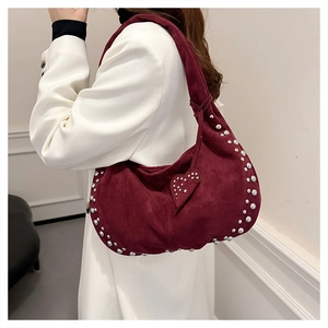 Detail of burgundy suede hobo bag with silver rivets and heart charm on a model
