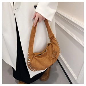Close-up of caramel suede crescent bag with silver rivets and heart charm on a model