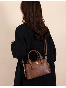 Side view of dark brown leather Boston bag worn on shoulder by a model in a black suit