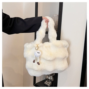 Close-up of white plush bucket bag with fuzzy ball charm held by a model in black blazer